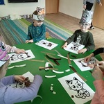 Dzieci przy stoliku wyklejają sylwetę kota papierkami.