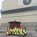 Grupa dzieci w kamizelkach odblaskowych stoi przed budynkiem Muzeum 