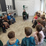 Dzieci siedzą w muzeum i słuchają opowiadania pani prowadzącej 