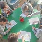 Dzieci siedzą przy stoliku i kolorują rysunki. 
