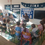 Dzieci siedzą na krzesłach i słuchają czytanego opowiadania 