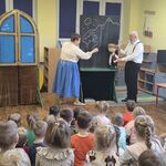 Aktor trzyma lalkę teatralną_ a pani aktorka wykonuje kredą rysunek na tablicy.