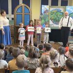 Czworo dzieci stoi koło aktorów_ trzymając kartki z obrazkami zwierząt.