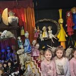 Grupa dziewczynek pozuje przy lalkach teatralnych.