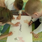 Kilkoro dzieci rysuje na dużej kartce z napisem Kwoka.