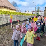 Dzieci stoją parami w ręku trzymając papierowe kwiaty.