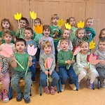 Grupa dzieci ustawionych w trzech rzędach trzyma kwiatki.