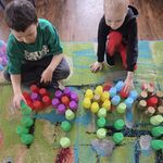 Dwóch chłopców układa kwiaty z kolorowych kubeczków na dywanie.
