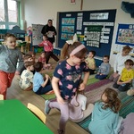 Kilkoro dzieci biegnie wokół kolegów siedzących na dywanie.