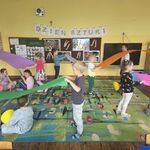 Dzieci stoją w parach trzymając bibułę_ niektóre dzieci siedzą na dywanie z kolorowymi kołami w rękach.