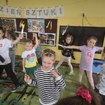 Dzieci stoją na dywanie z papierowymi pędzlami w rękach.