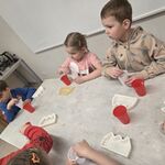 Dzieci stoją przy stoliku i mieszają substancję w kubeczkach.