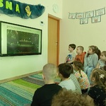 Przedszkolaki siedzą na dywanie i oglądają film.