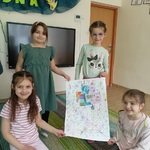 Kilka dziewczynek prezentuję swoją pracę plastyczną na dużym arkuszu papieru.