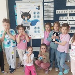 Grupa dzieci stoi przy plakacie Bofka_ na szyjach mają medale otrzymane za misję_ jedna z dziewczynek trzyma Bofka w dłoniach_