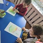 Dwóch chłopców siedzi przy stoliku i koloruje mapę Polski.