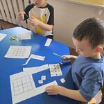 Dwóch chłopców siedzi przy stoliku i wycina elementy do sudoku.
