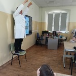 Dzieci obserwują mężczyznę stojącego na krześle i trzymającego dwa przedmioty.