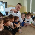 Przedszkolaki wykonują eksperyment z graniem na kieliszkach wypełnionych wodą.