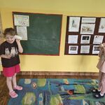 Dwie dziewczynki rozmawiają ze sobą trzymając papierowe kubeczki połączone sznurkiem.