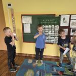  Dwóch chłopców komunikuje się poprzez telefon z kubeczków, obok nich stoją chłopcy którzy obserwują i dotykają napięty sznurek