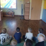 Dzieci siedzą na dywanie oglądają  edukacyjny 