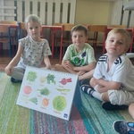 Kilkoro dzieci stoi pod tablicą trzymając narysowane przez siebie liście 
