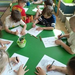 Przedszkolaki przy stoliku wykonują pracę plastyczną.