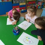 Trzy dziewczynki przy stoliku wykonują pracę plastyczną.