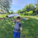 Chłopiec stoi_ trzyma rękę w górze_ w niej trzyma latawiec_ 
