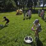 Dzieci stoją w dwóch rzędach_ dziewczynka i chłopiec wlewają wodę z kubeczka do misek.