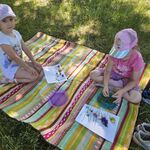 Dwie dziewczynki siedzą na kocu i układają na kartkach kompozycje z roślin.
