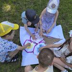 Grupa dzieci siedzi wokół dużej kartki i rękami miesza piankę z farbami na konturze lodów.