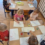 Dzieci siedzą przy trzech stolikach wykonując prace plastyczne na dzień kropki.