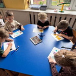 pięcioro dzieci rysuje kredkami siedząc przy stoliku.
