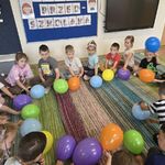 Dzieci siedzą w kole jeden za drugim_ a balony leżą wewnątrz koła.