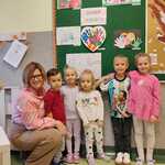 5 uśmiechniętych dzieci_ przy nich pani_ w tle tablica z wywieszonymi pracami plastycznymi