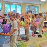 Dzieci w parach  stoją na dywanie. Trzymają się za ręce_ między nimi balony z uśmiechem.