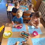  Dzieci siedzą przy stolikach robiąc prace plastyczne.