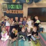 Grupa przedszkolaków pozuje przy napisie Dzień Drzewa.