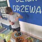 Chłopiec stoi przy stoliku z naturalnymi okazami przyrody i przelewa zabarwioną wodę do kubeczka.