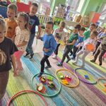 Dzieci ustawione parami znajdują się na dywanie wokół kolorowych obręczy.
