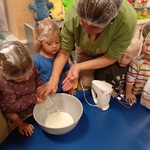 Koledzy patrzą jak dziewczynka wsypuje mąkę do miski.