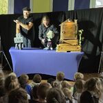 Aktorzy stoją naprzeciwko dzieci trzymając pacynki robota i królika.