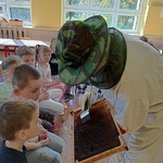 ubrany w strój ochronny pszczelarz pokazuje dzieciom przyrządy do wydobywania miodu