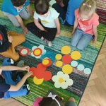 dzieci siedzące na dywanie i układające różne kształty z kolorowych kropek