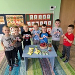 Grupa chłopców trzyma obrazki z jabłkami stojąc przy stole na którym znajdują się jabłka w różnej postaci.jpg