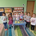Grupa dziewczynek trzyma obrazki z jabłkami, przy stole na którym znajdują się jabłka w różnej postaci.jpg