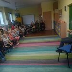 na zdjeciu funkcjonariuszka służby więziennej czytajaca ksiązkę, w tle dzieci i inni funkcjonariusze.jpg