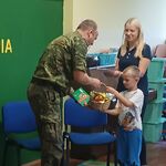na zdjęciu dziecko i kobieta wręczający strażnikowi granicznemu koszyk z jabłkami.jpg